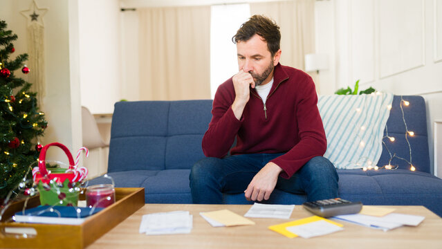 Fototapeta Man anxiously bites his nails while tallying up his holiday spending at home