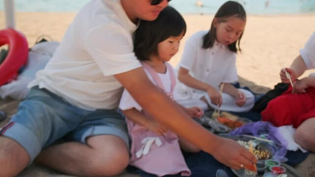Time on holiday with the whole family on the beach snacking on sushi rolls in food delivery boxes from a Japanese restaurant.