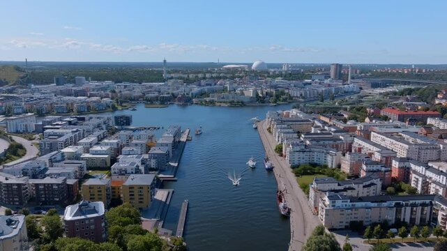 Boats sail along a canal in Stockholm, showcasing modern buildings, the tv tower, and the Ericsson Globe. Vibrant urban landscape reflects the city's unique charm