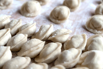 The raw dumplings were placed on a wooden cooking board, sprinkled with flour. The filling is minced meat, potatoes, cheese or cottage cheese. A semi-finished product, ready for cooking.