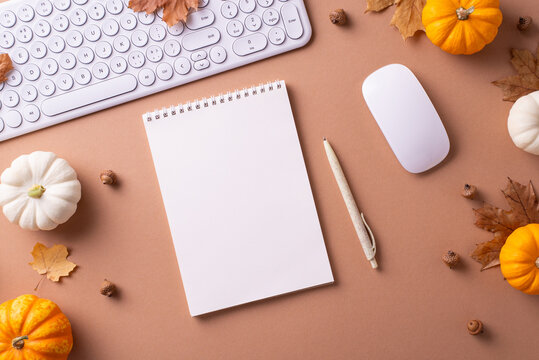 Flat lay of an autumn themed workspace featuring a keyboard, mouse, notepad, pen, and mini pumpkins to evoke creativity and seasonal warmth