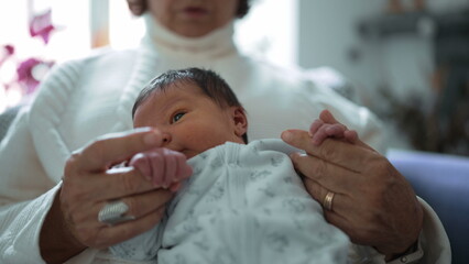 Fototapeta premium Grandmother tenderly gazing at her newborn grandchild, capturing a moment filled with love, care, and the special bond between the elder and the newest member of the family
