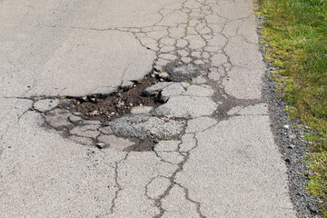 Seitenstraße mit Schäden an der Asphaltdecke, insbesondere einem Schlagloch (Ausbruch) und...