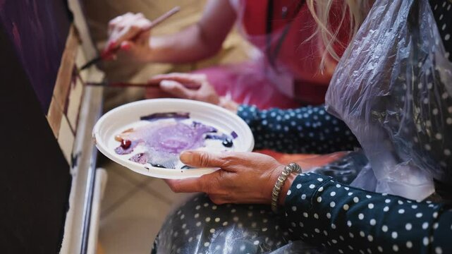 Process of drawing with brush, group class of talented students with painting easels and canvases during lesson of watercolour painting in auditorium, drawing class for adult artists in art school,