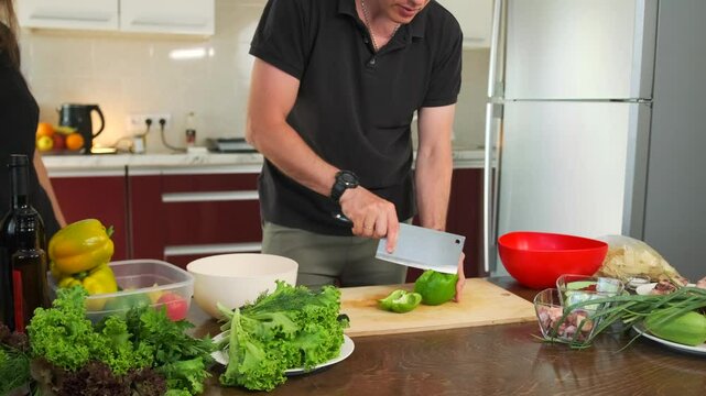A man carefully slicing a bell pepper with a sharp knife standing at a kitchen counter in his apartment preparing dinner.