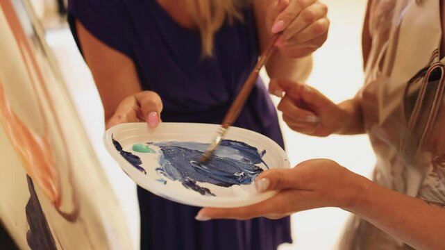 Process of drawing with brush, group class of talented students with painting easels and canvases during lesson of watercolour painting in auditorium, drawing class for adult artists in art school,