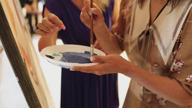 Process of drawing with brush, group class of talented students with painting easels and canvases during lesson of watercolour painting in auditorium, drawing class for adult artists in art school,