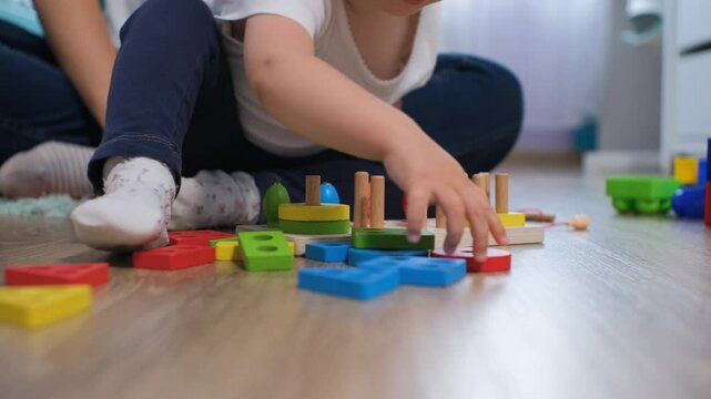 Close-up of mother engages with her baby daughter as they explore colorful wooden toys in a cozy nursery, fostering creativity and learning through playtime together