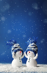 Two little snowmen in caps on snow in the winter. Background with a funny snowmen. Christmas card.