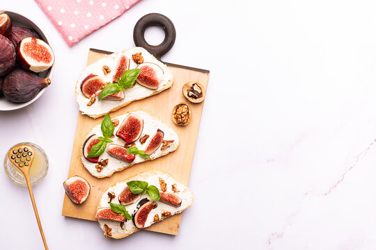 Tasty homemade sandwiches with sweet figs, cream cheese, walnuts. honey and mint leaves on the wooden serving plate on light marble background close up.