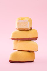 Slices of cheesecake cut in half covered with yellow chocolate velour on pink background with copy space. 