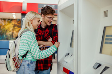Smiling traveling couple using ticket machine at train station.