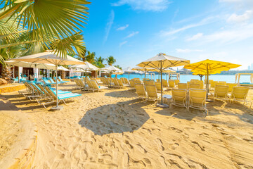 Lounge chairs, palm trees and huts along a sandy beach and resort on Palm Jumeirah island, on the Arabian Gulf at Dubai, United Arab Emirates.