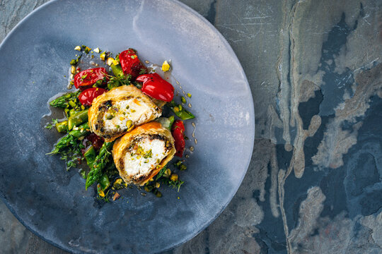 Traditional Turkish crispy sigara b&ouml;rek rolls stuffed with goat cheese in filo pastry and served with tomatoes and green asparagus as top view on a Nordic design plate with copy space right