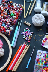 Colorful beads, coloring pencils, glitter, needles, string, hoop, tape and scissors on dark...
