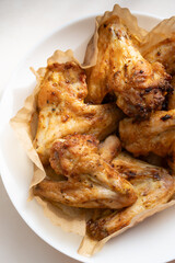 Homemade meal cooked in air fryer grill. Freshly fried chicken wings are placed on paper in white plate with the light shining through the window falling on the chicken Selective focus, vertical photo