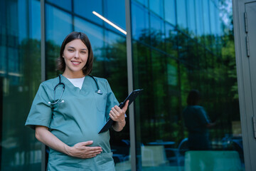 Pregnant young doctor on the clinic building background