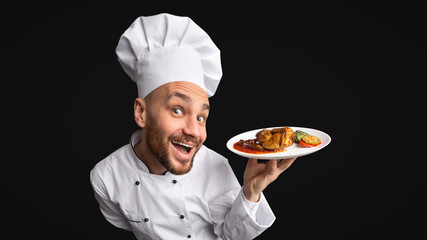 Funny Chef Cook Man Showing Chicken Dish On Plate Posing On Black Background. Panorama, Studio Shot