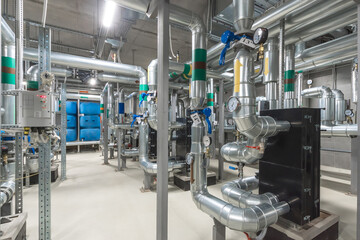 Complex arrangement of stainless steel pipes, valves, and gauges inside a well-lit industrial...