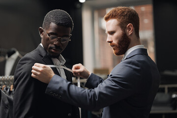 Tailor measuring client for bespoke suit. Young man African American businessman in tailoring studio