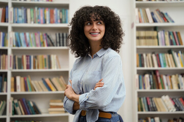 Curly-haired pretty young woman standing on the bookshelves background