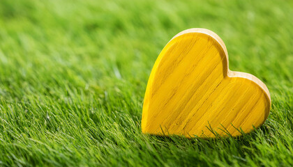 Yellow wooden heart shape on fresh green grass. Eco-friendly lifestyle and clean environment.