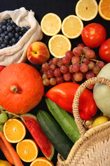 Round straw bag and various seasonal fruits and vegetables on dark background. Summer and fall produce. Top view.