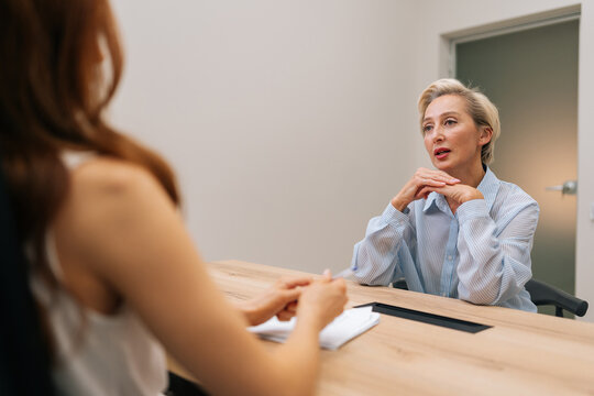 Serious mature adult female business project leader interviewing young woman job candidate. Gray-haired successful businesswoman interviewing candidate on job interview in conference room.