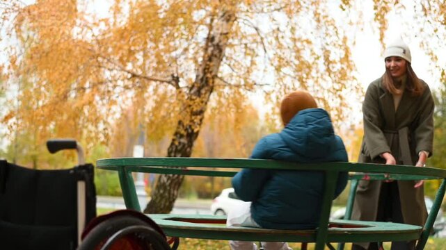 mother with disabled child in disabled Kremlin walk in autumn on the playground on the carousel. High quality FullHD footage