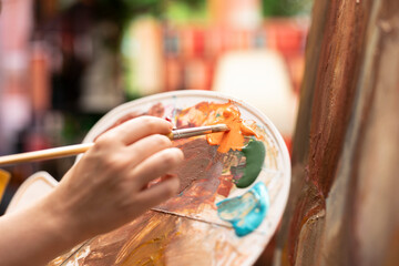 Talented artist painting an artwork with colorful paints mixed on a palette, creating a beautiful creative paintwork with a painting technique in her atelier. Painter mixing watercolor. Close up.