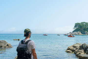 a man looking out to sea with a backpack on his back.a man looking out to sea with a backpack on his back.