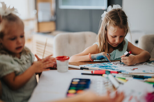 Two young sisters engage in colorful art activities at home. They are focused and enjoying time together creating beautiful artwork. Perfect for themes of creativity, childhood, and sibling bonding.