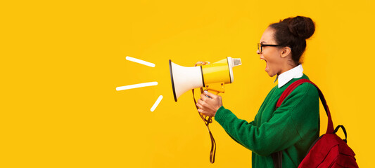 Attention. Black teen girl with megaphone screaming isolated over yellow background, panorama