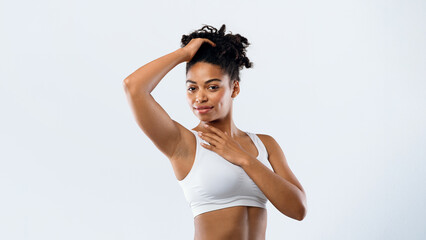 Obraz premium Pretty afro woman in underwear smelling her fresh armpit over grey background, putting hand up, copy space, advertisement for under arm epilation