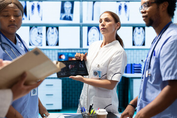 Obraz premium Diverse doctors team looking at radiography scan test result to check organs condition, examining liver and lungs to fight illness. Group of physicians discussing healthcare services for wellness.