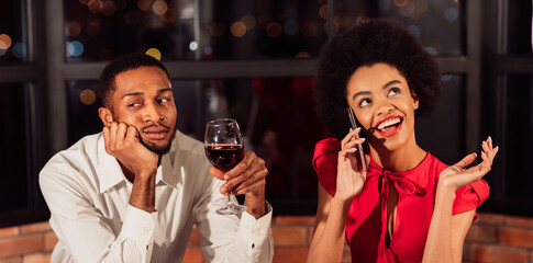 Bad Date. Bored Black Man Waiting While His Girlfriend Talking On Phone Having Romantic Dinner In Restaurant.