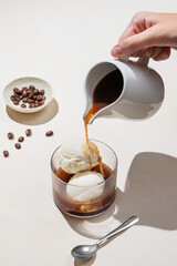 Affogato coffee with vanilla ice cream scoops and  espresso poured into a glass on a light background with coffee beans and shadow.