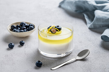 Creamy lemon panna cotta with blueberries in a glass  with fresh berries, spoon and napkin on a light background.