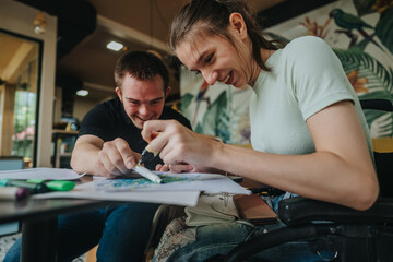 A young man with Down syndrome and a girl in a wheelchair share a joyful moment as they draw and paint together, showcasing creativity, friendship, and inclusion.