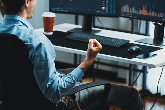 Cropped successful young stock trader calling on smartphone to business partner with dynamic financial investment screen with coffee cup on desk at modern office, trading currency theme. Gusher.