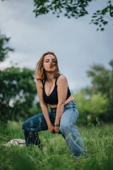 Confident young woman in casual attire posing in a lush green field with cloudy skies in the background, expressing freedom and self-assurance.