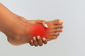 Cropped of black woman holding her painful foot, cramp, muscular spasm, red accent on sore zone