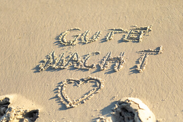Good night message written in the sand on a beach during sunset, with gentle waves lapping at the shore, creating a peaceful atmosphere