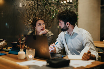 Two business professionals work together late at night in a coffee bar, collaborating on a project and catching a deadline.