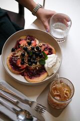 Delicious brunch plate with fluffy pancakes topped with strawberries, blueberries, granola, and whipped cream. Served with iced tea and a glass of water, offering a wholesome breakfast experience.