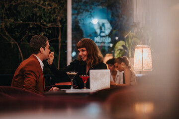 A loving couple shares a joyful moment during a romantic evening at a stylish restaurant with dim...
