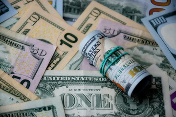 Hundred dollar bills roll lies on big amount of US dollars in different nominations under natural light