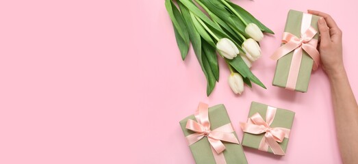 Female hand, gift boxes and beautiful white tulips on pink background with space for text, top view