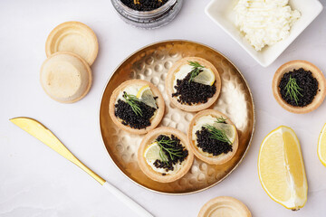 Plate of tasty tartlets with black caviar on grey background