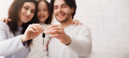 Housing concept. Happy family with little daughter holding key from their new flat, selective focus on hands, closeup.